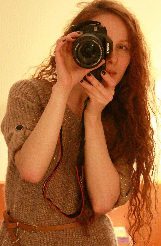 Elena holding a Canon camera in a warm self-portrait